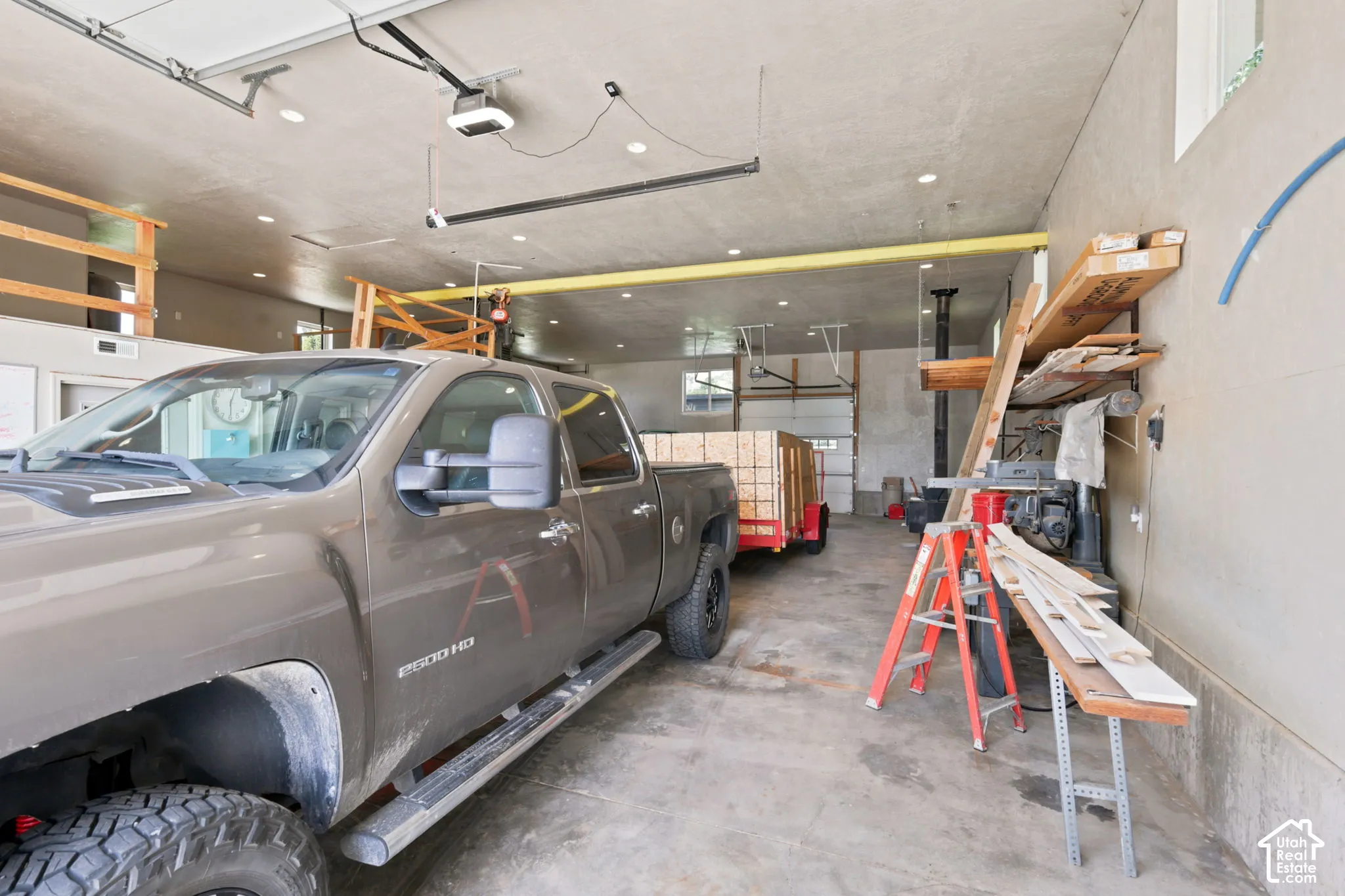 Spacious garage featuring a concrete floor, multiple automatic garage doors, abundant overhead lighting, high ceilings, and an exposed overhead beam