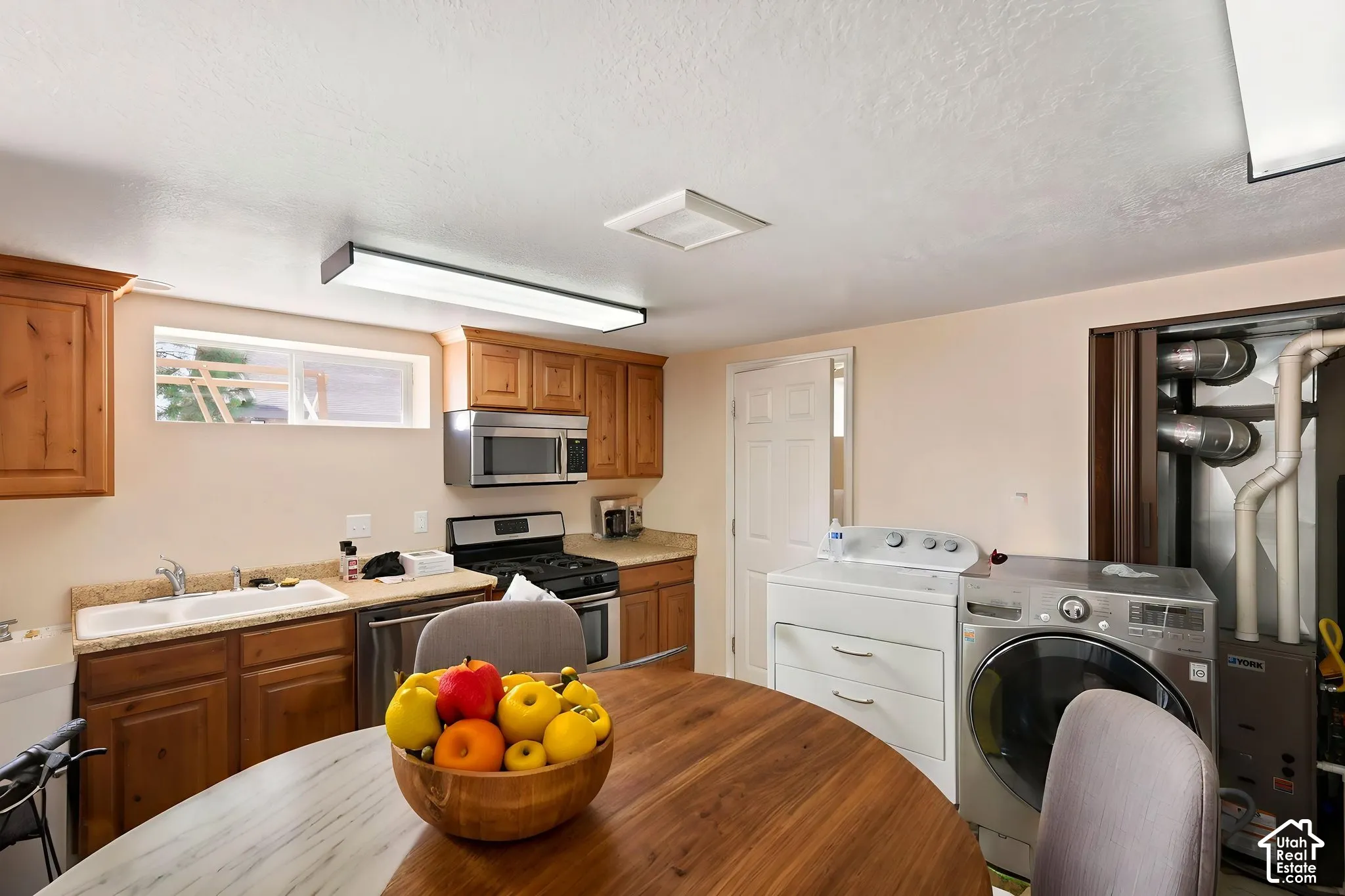 Kitchenette featuring wood-finish cabinetry, light-toned countertops, and a stainless steel appliance suite including a gas range and microwave  Digitally staged.
