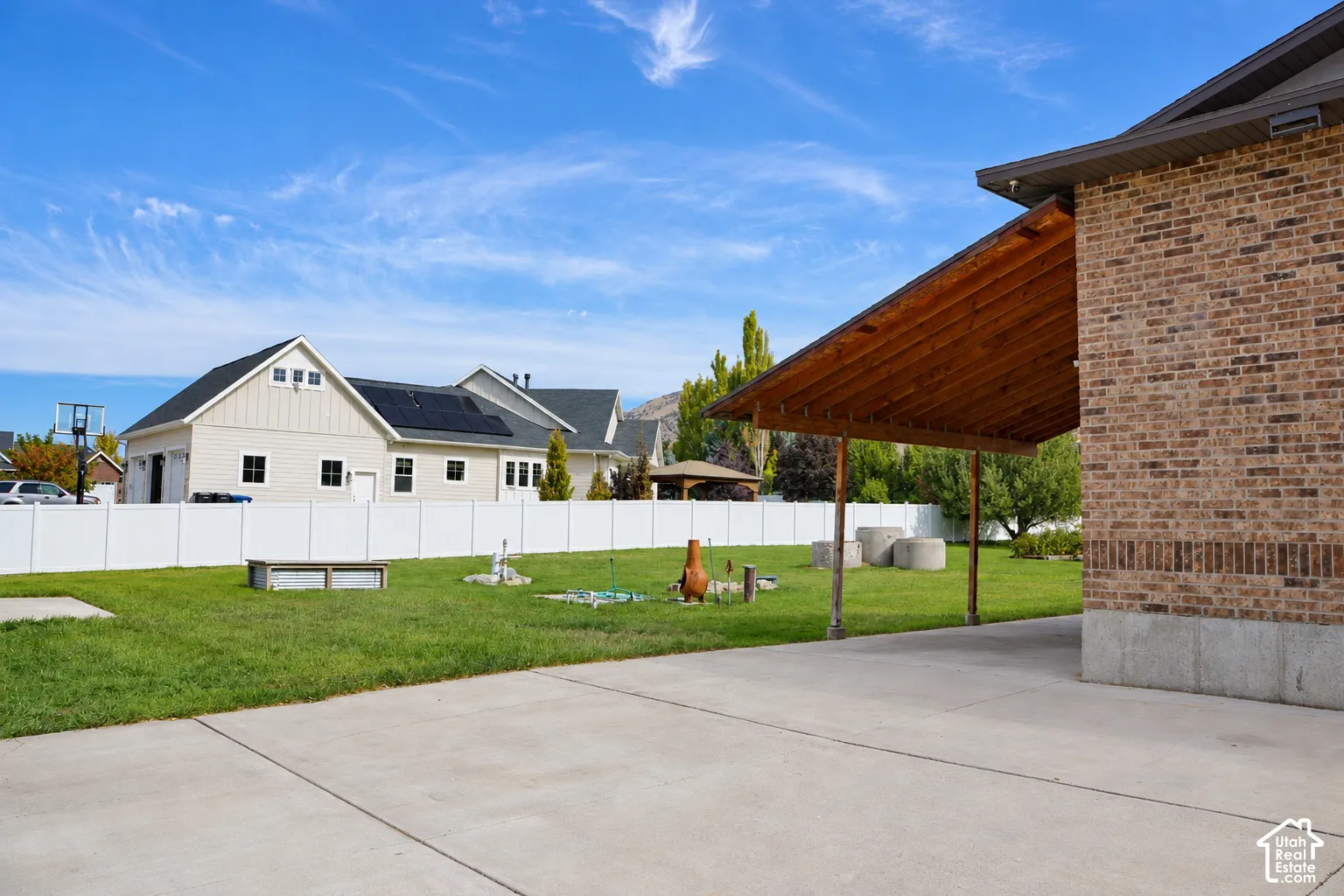Brick exterior with covered patio featuring exposed wood beams, concrete patio, and expansive green lawn