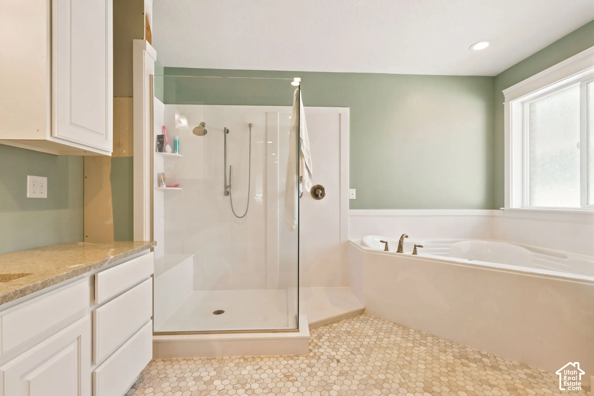 Bathroom featuring a built-in soaking tub, a glass-enclosed shower with a bench, and a vanity with a light-toned   Digitally staged.