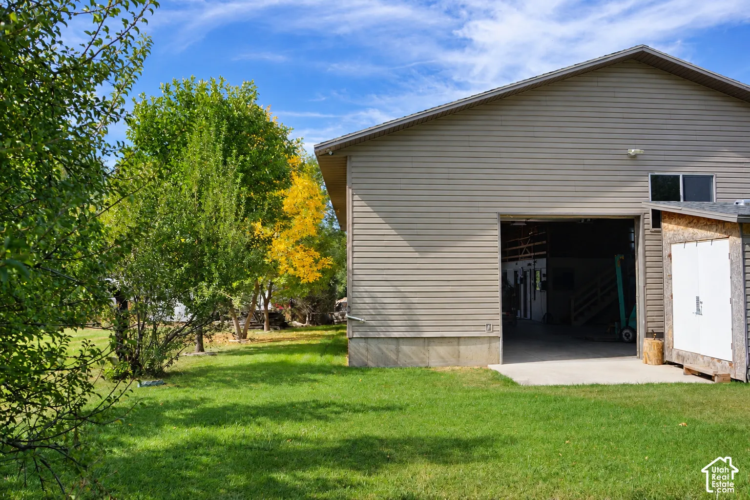 Siding exterior with an open bay door, concrete pad, and a separate storage shed