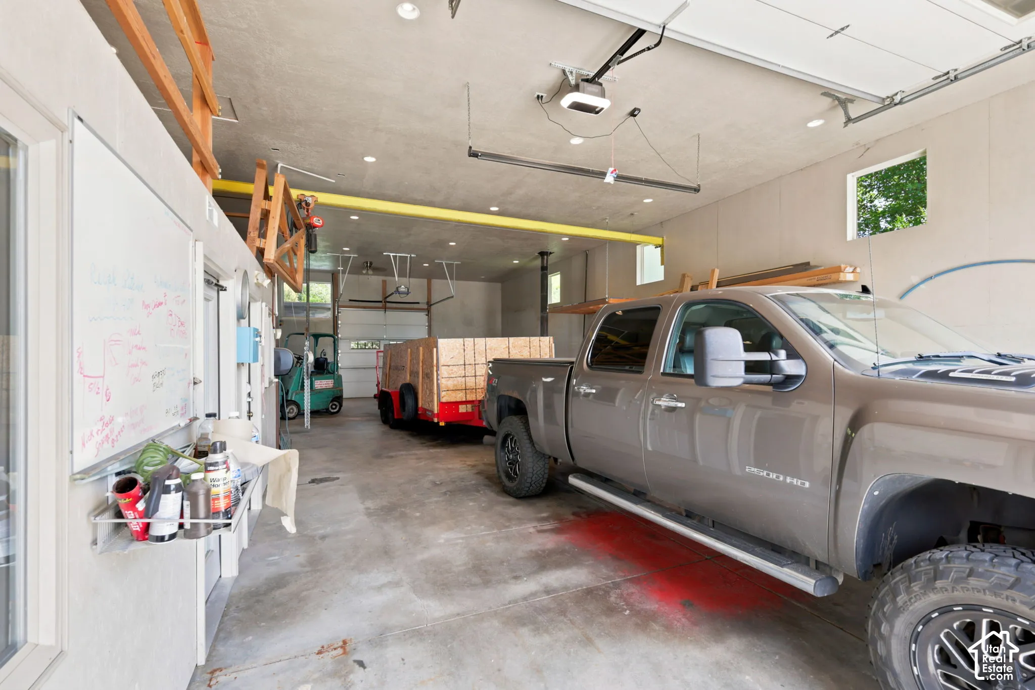Spacious concrete-floored garage featuring multiple overhead doors, high ceilings with exposed beams, and recessed lighting