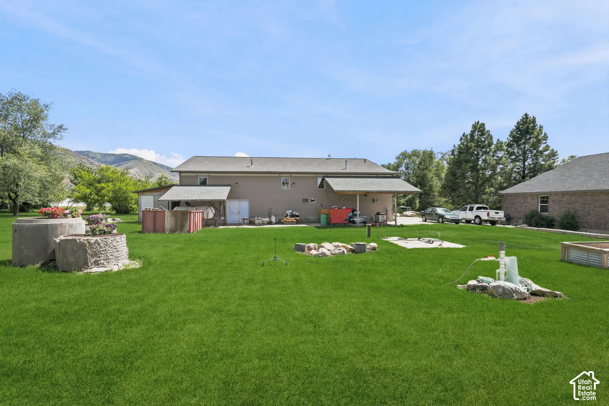 Expansive lawn area featuring a multi-level concrete planter, a covered patio structure, and a raised garden bed