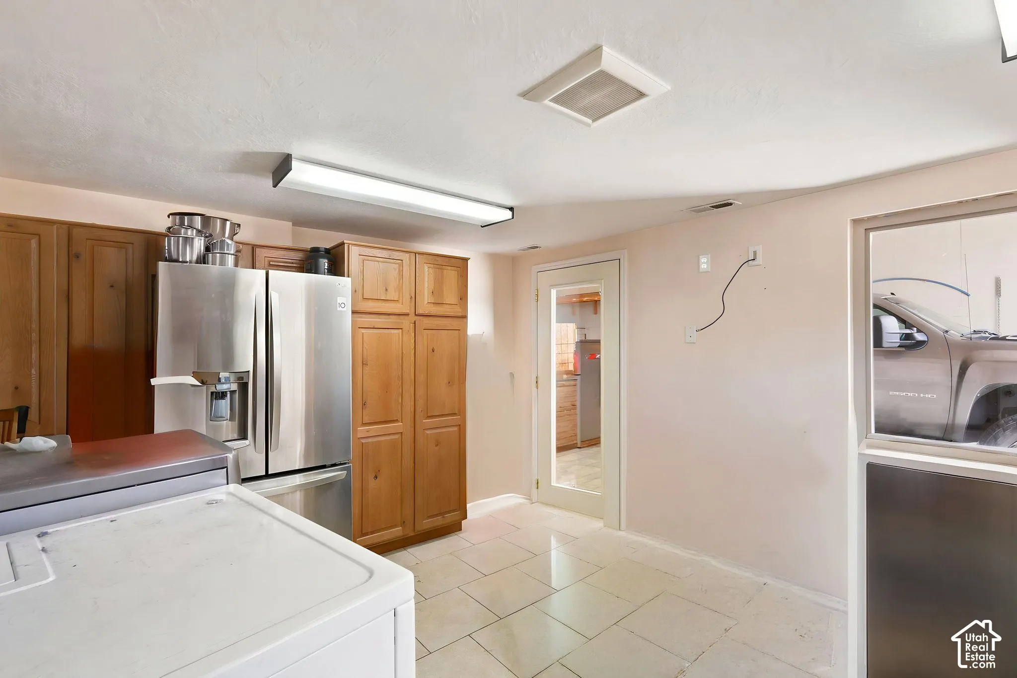 Kitchen area featuring wood cabinetry, stainless steel refrigerator, and tile   Digitally staged.