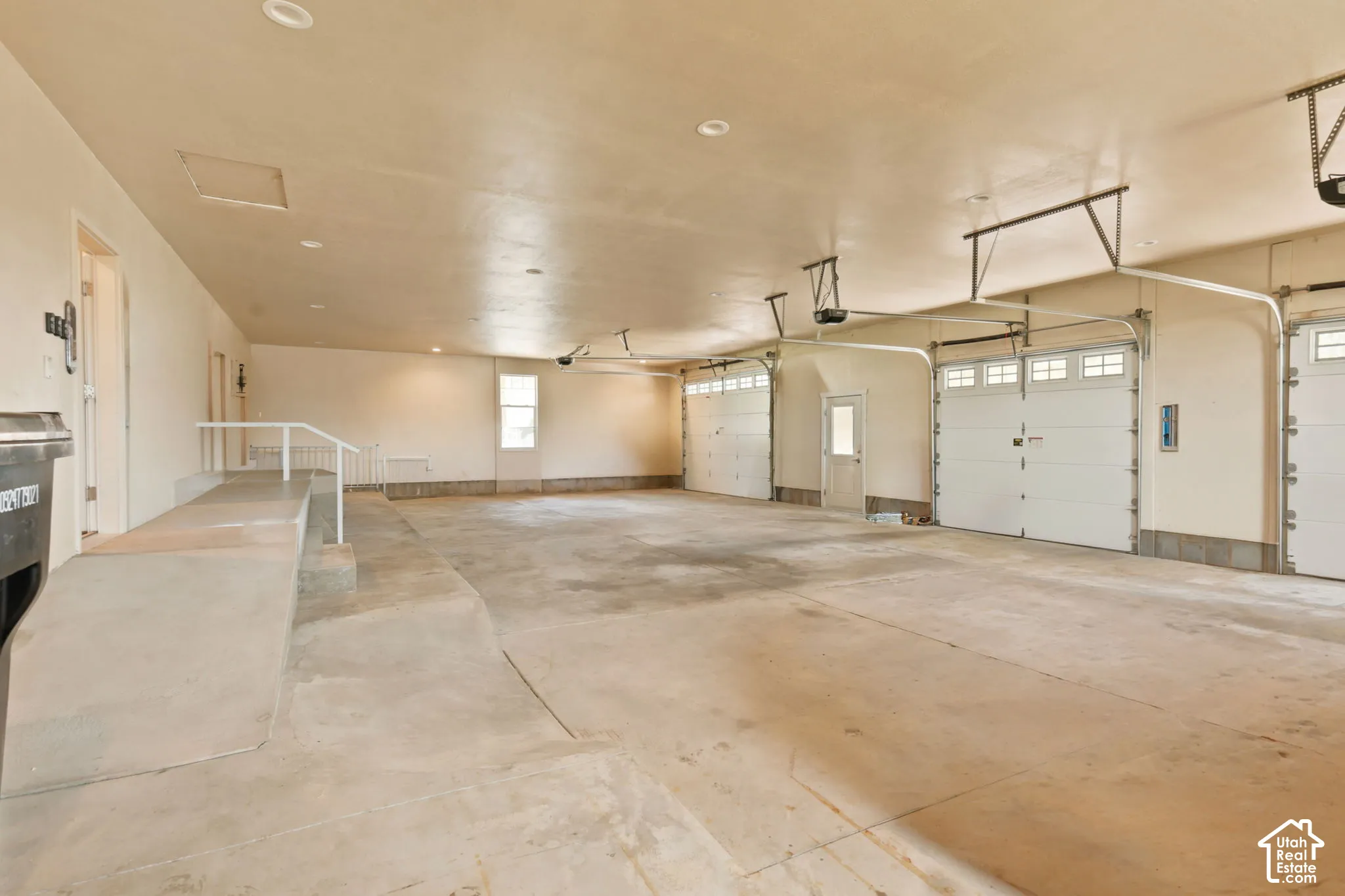 Spacious multi-car garage featuring multiple overhead doors with windows, ample interior lighting, a built-in access ramp with handrail, and a window for natural light