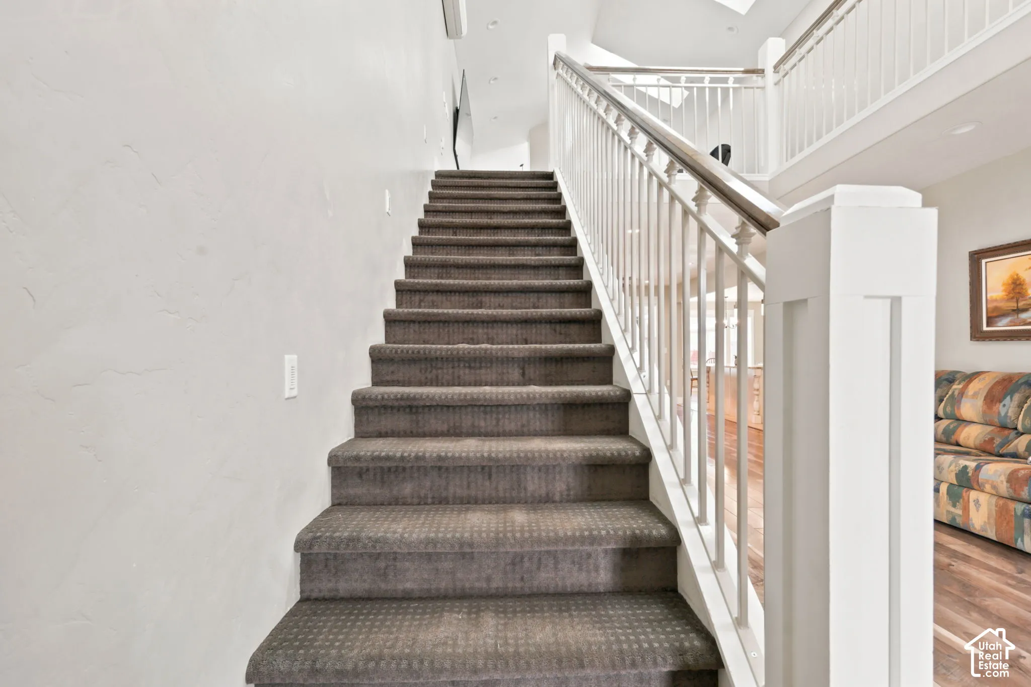 Carpeted staircase with white balusters and a wood-finish handrail leading to an upper level.