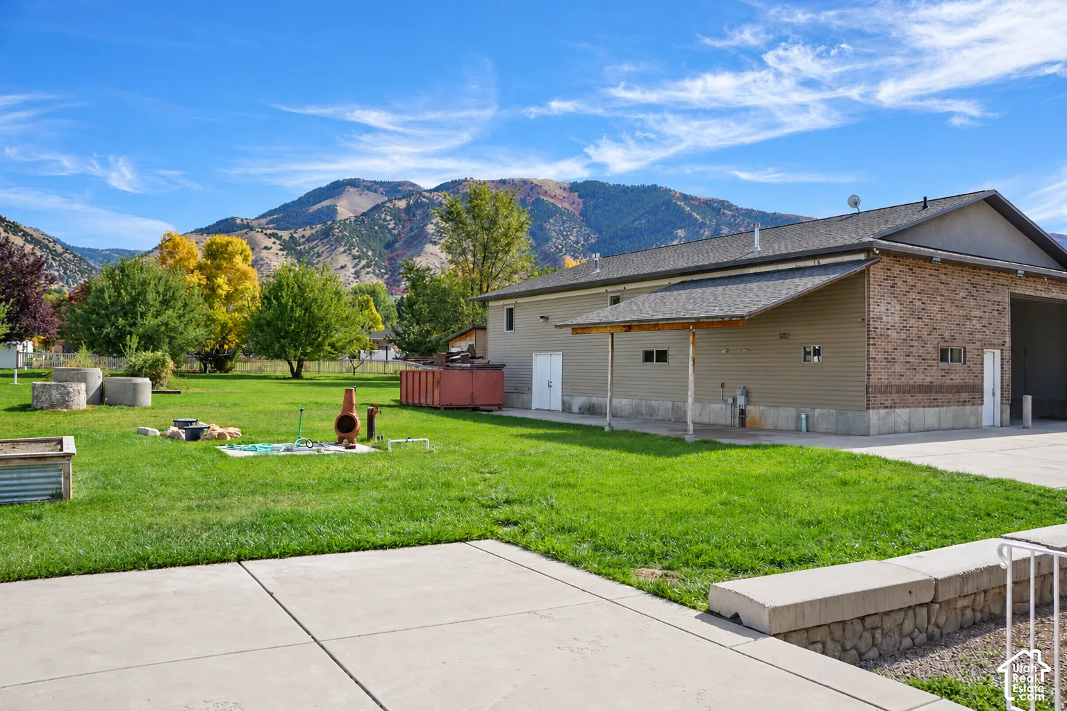 Expansive concrete patio with a retaining wall, overlooking a large grassy area with mature trees and mountain scenery