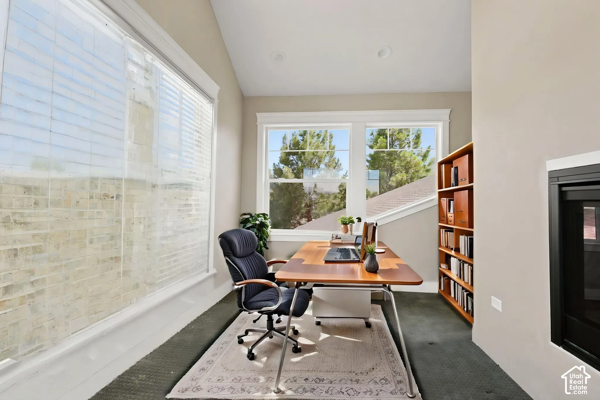 Bright interior space featuring multiple windows, sloped ceiling, recessed lighting, and a built-in fireplace with a black surround  Digitally staged.