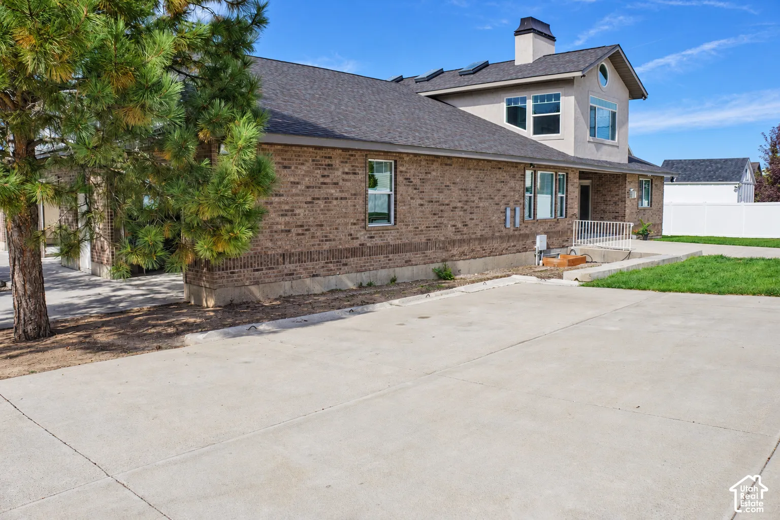 Brick exterior with stucco accents, dark shingle roof, multiple windows, and a paved concrete surface
