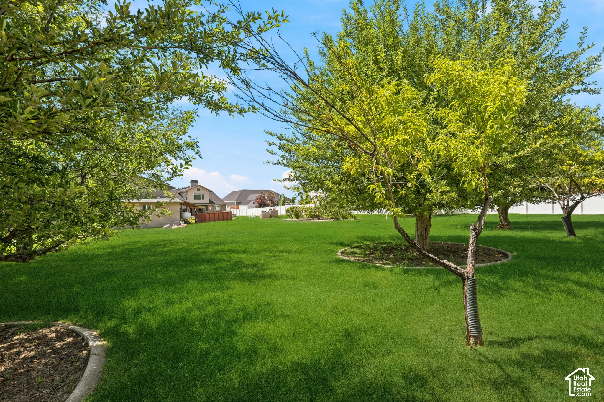 Expansive lawn area featuring mature trees with mulched bases and a perimeter   Digitally staged.
