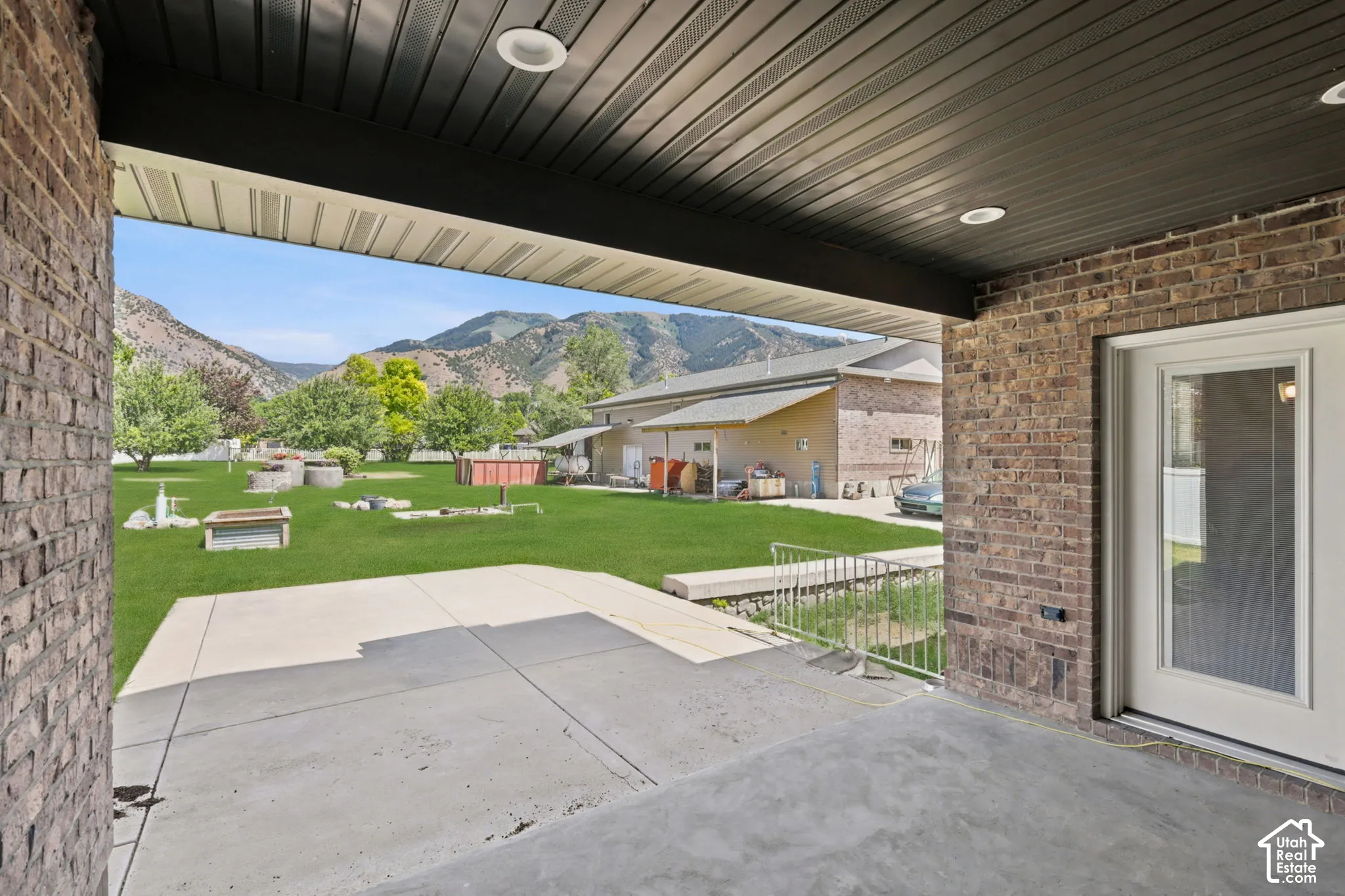 Covered patio with recessed lighting, brick exterior, and direct access to a large grassy area.