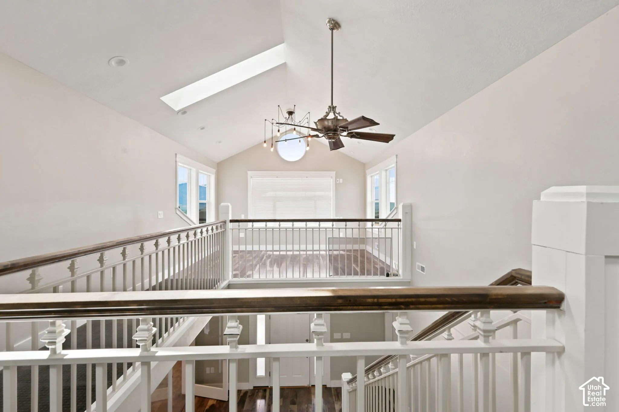 Upper-level landing featuring vaulted ceilings, a skylight, and an overhead light fixture with a ceiling fan