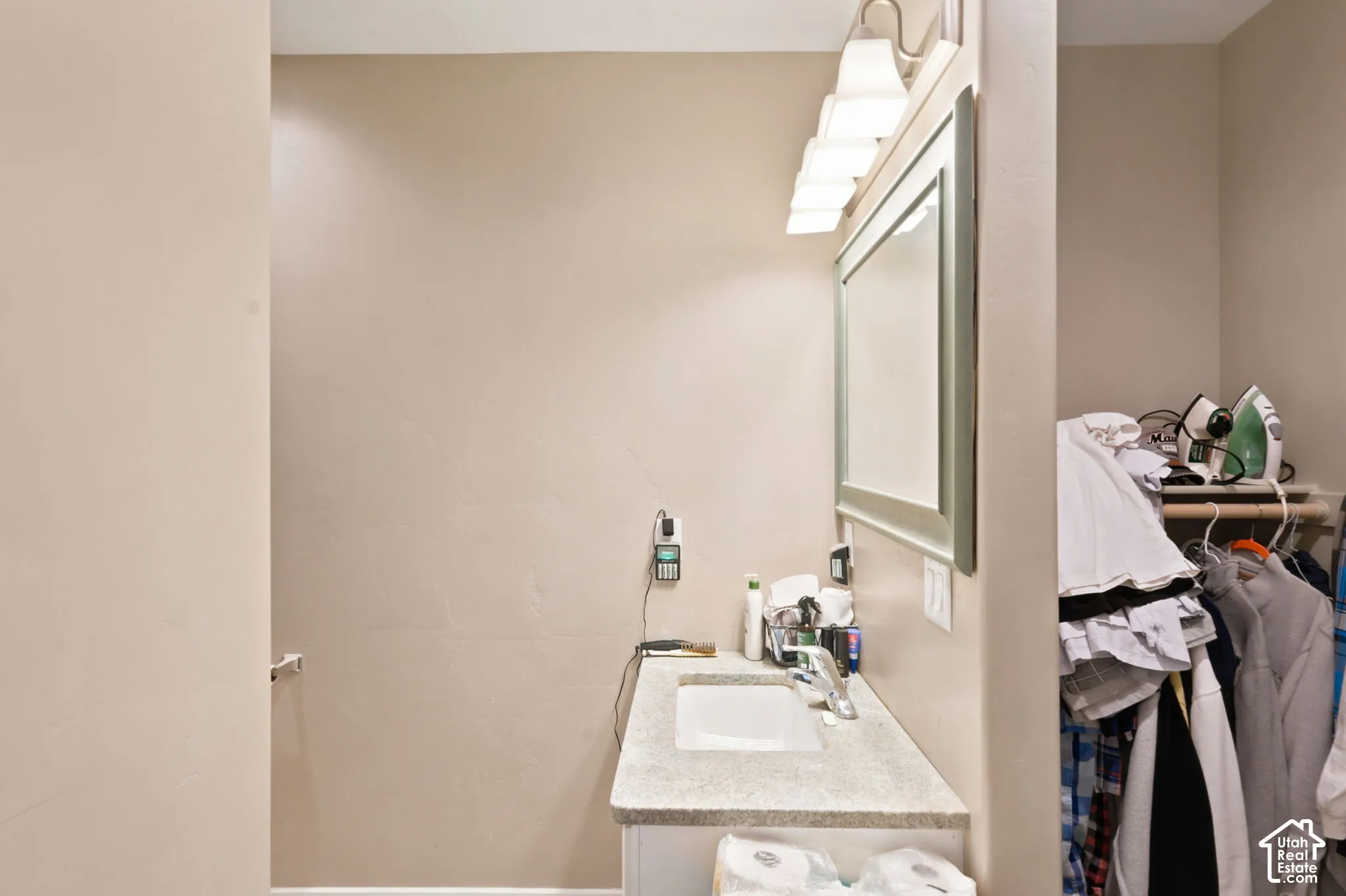 Vanity area featuring a light-toned countertop with an integrated sink, a large framed mirror, and a five-light fixture  Digitally staged.