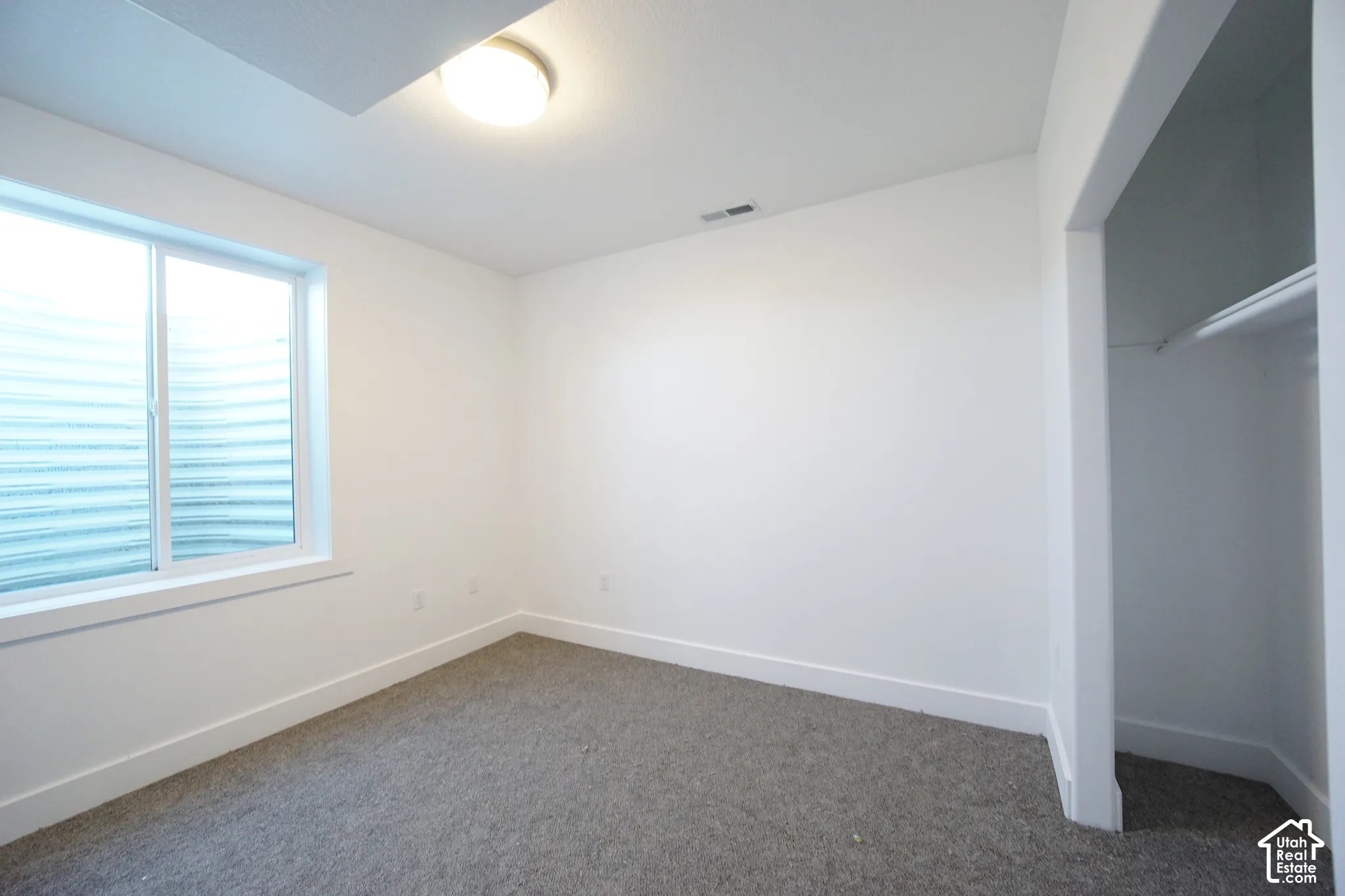 Recessed window, white trim, wall-to-wall carpeting, built-in closet with hanging rod, overhead flush-mount lighting