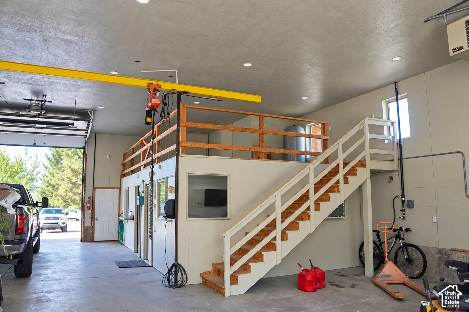 High-bay garage with overhead door, exposed beam crane system, and a mezzanine level featuring a wood-railed staircase