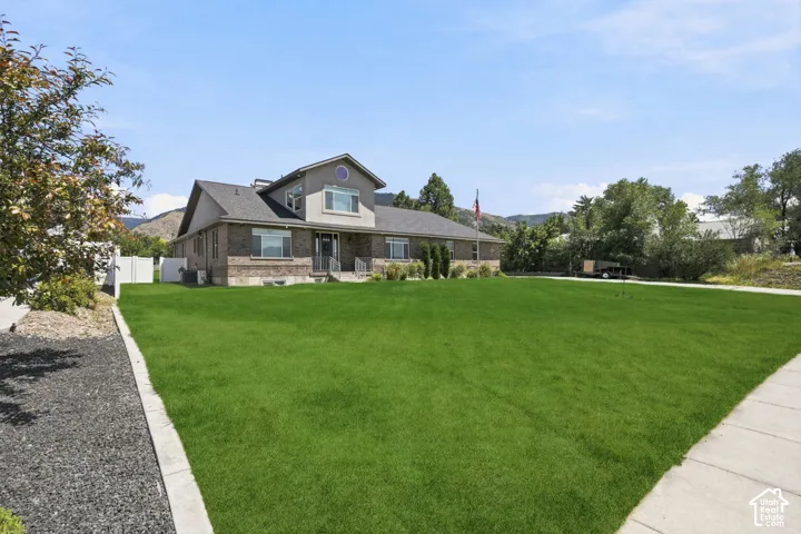 Expansive green lawn and concrete pathway fronting a brick and stucco residence featuring a prominent gabled roofline  Digitally staged.