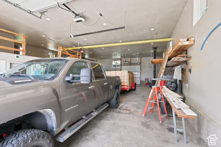 Spacious garage featuring a concrete floor, multiple automatic garage doors, abundant overhead lighting, high ceilings, and an exposed overhead beam