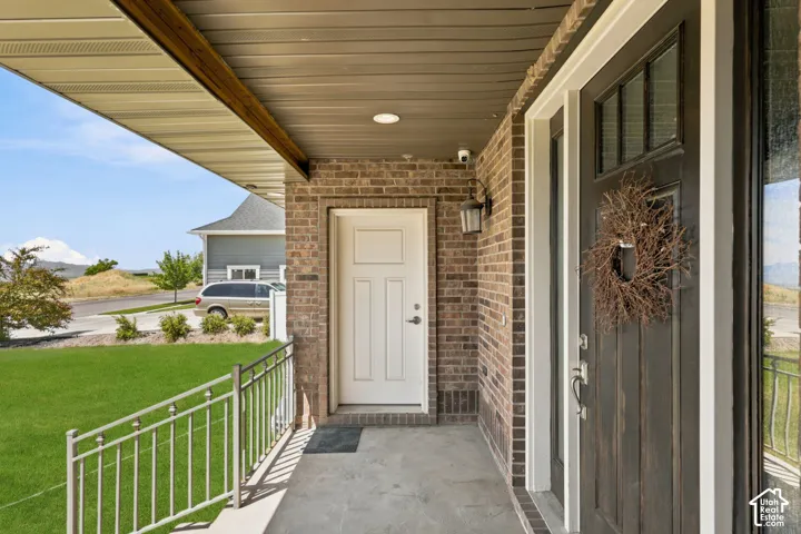 Brick facade entryway featuring a dark wood-finish front door with glass transom, a white paneled door, a concrete porch, and a metal railing