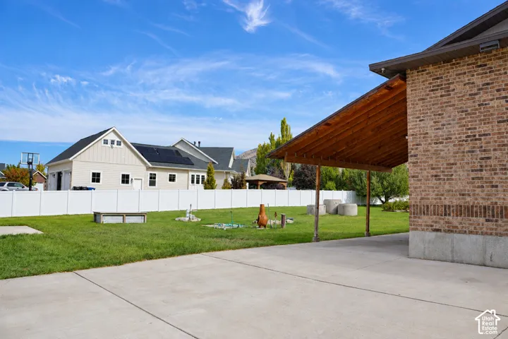 Brick exterior with covered patio featuring exposed wood beams, concrete patio, and expansive green lawn