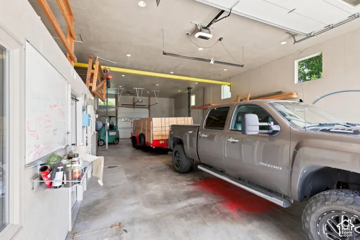 Spacious concrete-floored garage featuring multiple overhead doors, high ceilings with exposed beams, and recessed lighting
