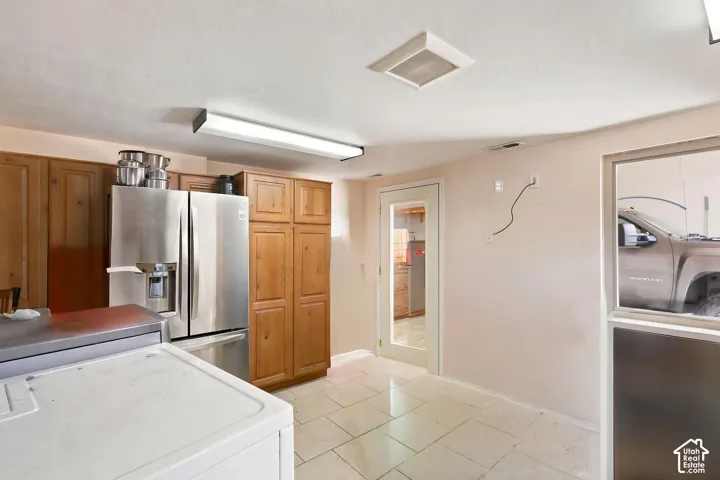 Kitchen area featuring wood cabinetry, stainless steel refrigerator, and tile   Digitally staged.