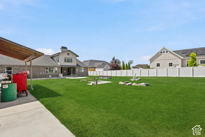 Expansive grassy backyard featuring a paved patio, a white privacy fence, and a covered patio   Digitally staged.