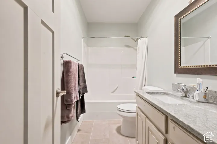 Bathroom featuring a white tub and shower combination, a vanity with a light-colored countertop and integrated sink, a large framed mirror, and light-toned floor tiles