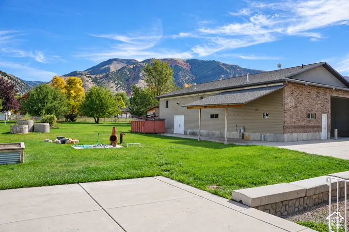 Expansive concrete patio with a retaining wall, overlooking a large grassy area with mature trees and mountain scenery