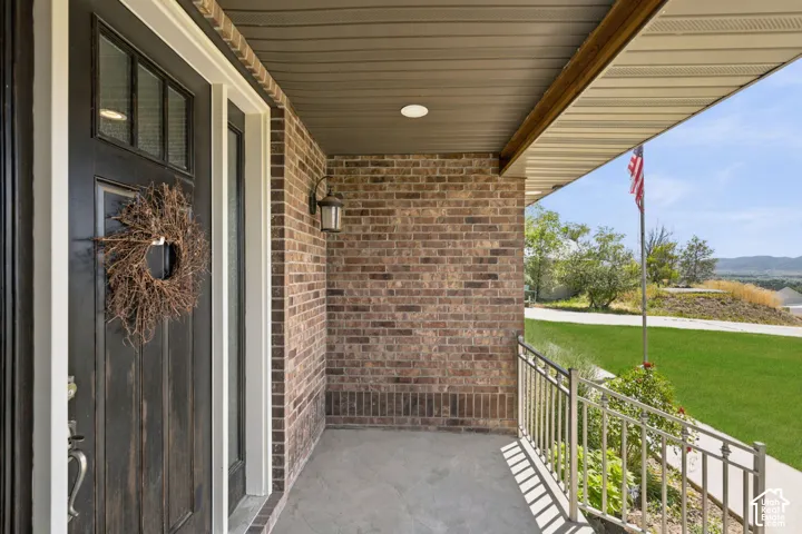 Covered front porch featuring brick siding, a dark wood-finish entry door, an overhead light fixture, and a metal handrail
