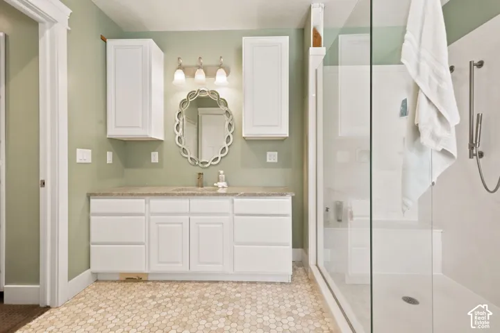 Bathroom featuring a clear glass shower enclosure with a built-in bench, hexagon tile flooring, a single vanity with stone-finish countertop, white cabinetry, and a decorative wall.   Digitally staged.
