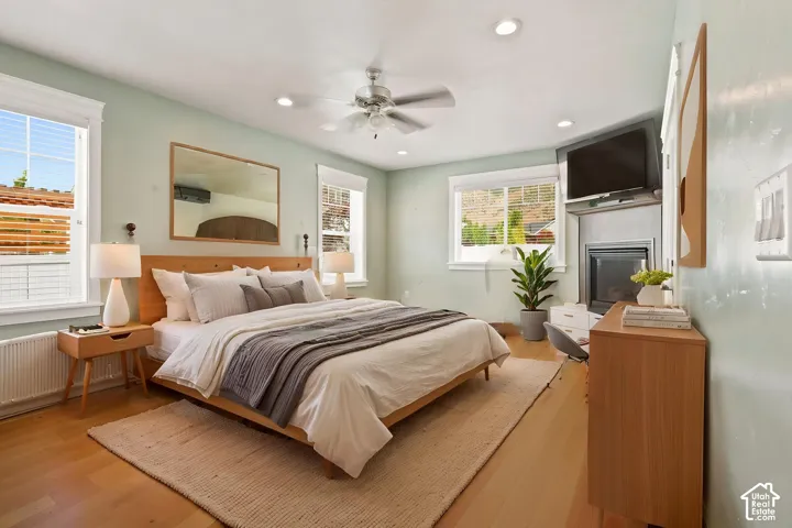 Hardwood flooring and light green walls frame a bedroom featuring a built-in fireplace with a television   Digitally staged.