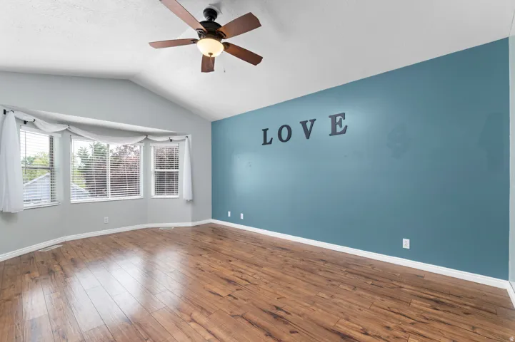 Primary Bedroom Suite Vaulted ceiling with a ceiling fan, bay window with blinds, wood-finish flooring, and a contrasting accent wall