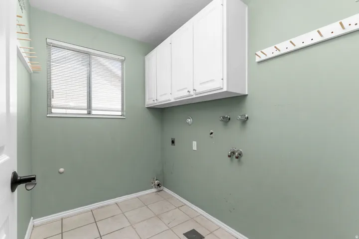 Utility room featuring tile flooring, a window with blinds, and white upper cabinetry