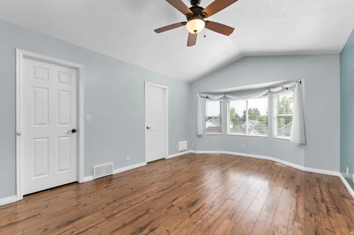 Primary Bedroom Suite Vaulted ceiling with a ceiling fan, bay window with blinds, wood-finish flooring, and light blue wall tones