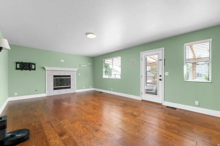 Hardwood-finish flooring throughout, featuring a tiled fireplace with mantel, multiple windows, and a glass-paneled exterior door