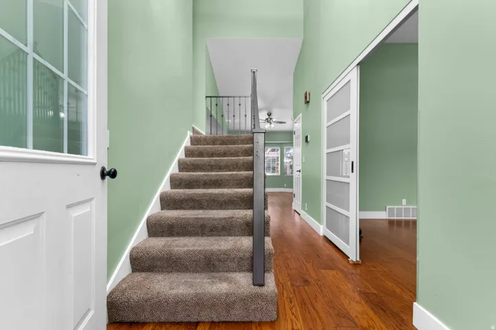Wood-finish flooring, carpeted staircase with metal handrail, sliding barn door, and high ceilings