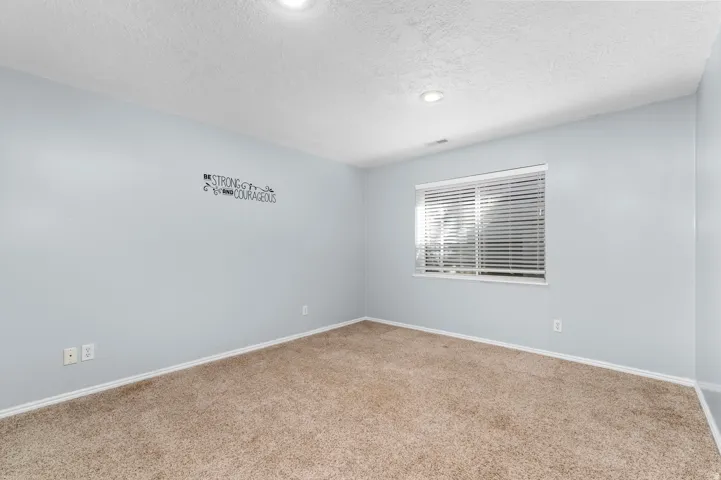 Recessed ceiling lighting, textured ceiling, light blue wall paint, window with blinds, and brown carpet flooring