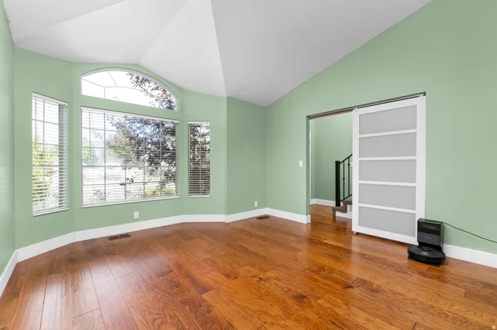 Vaulted ceiling, bay window, arched transom window, wood-finish flooring, and a modern sliding barn door