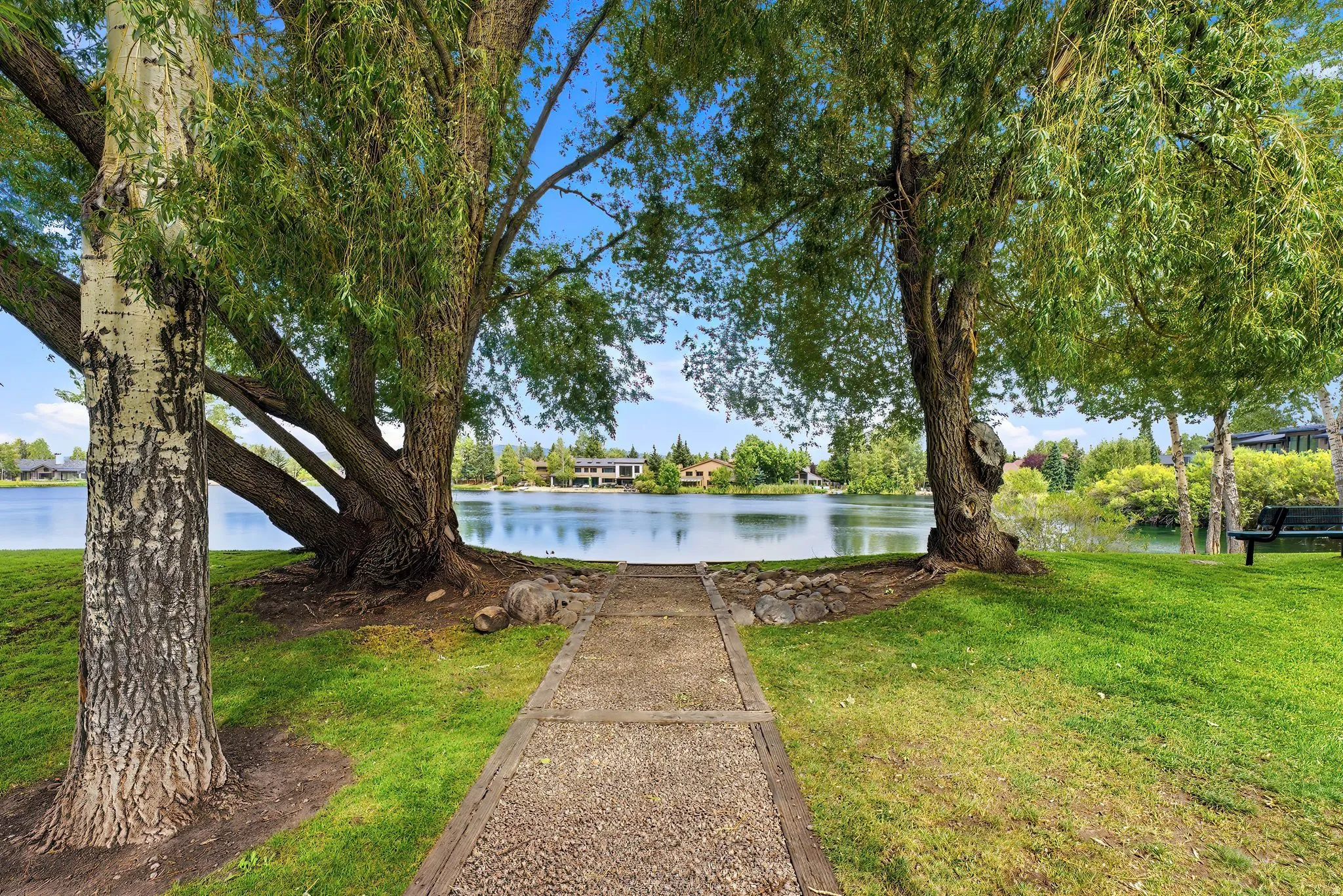 Manicured lawn with mature trees and a paved pathway leading to the water's edge