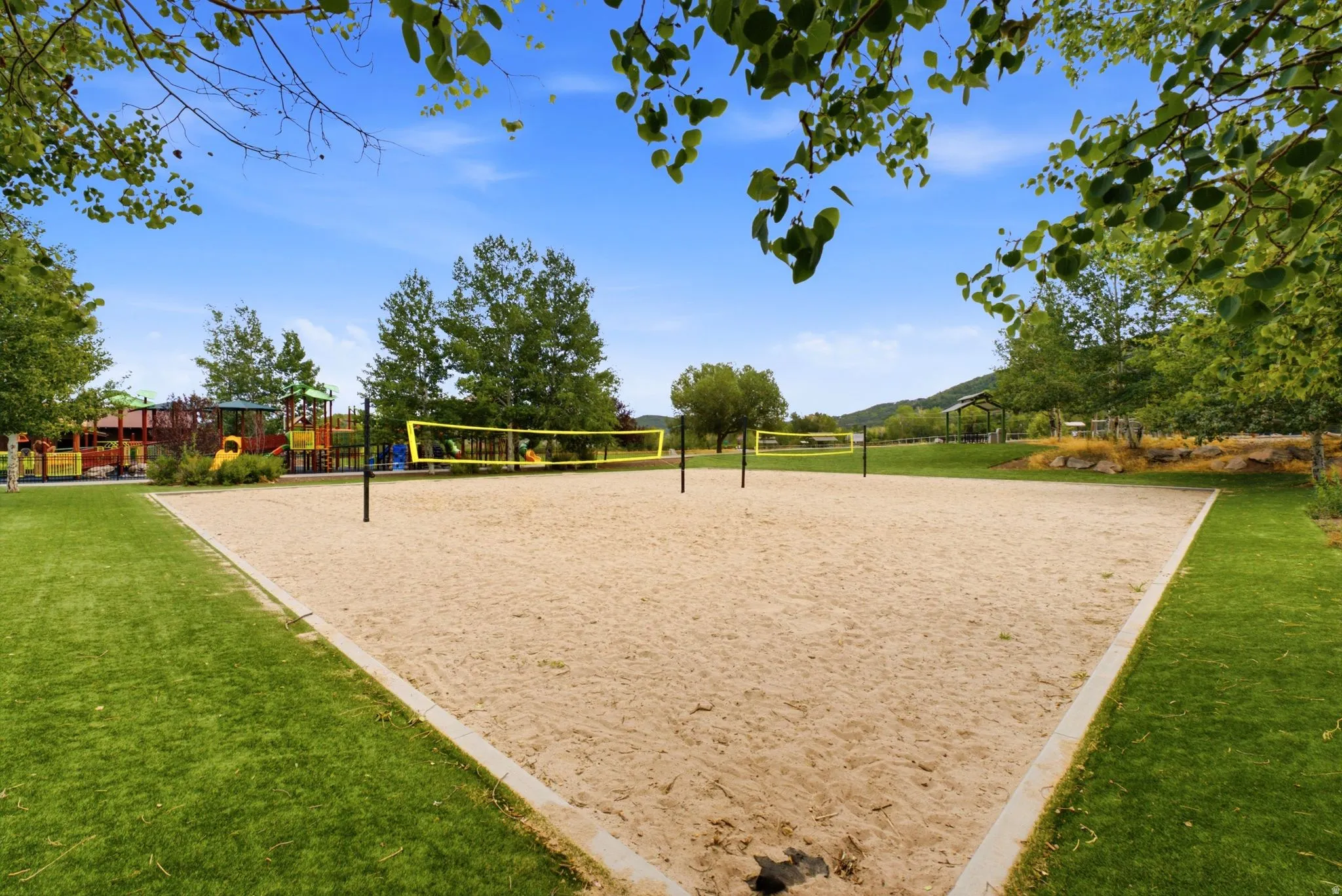 Sand volleyball court with surrounding green space, playground equipment, and distant mountains