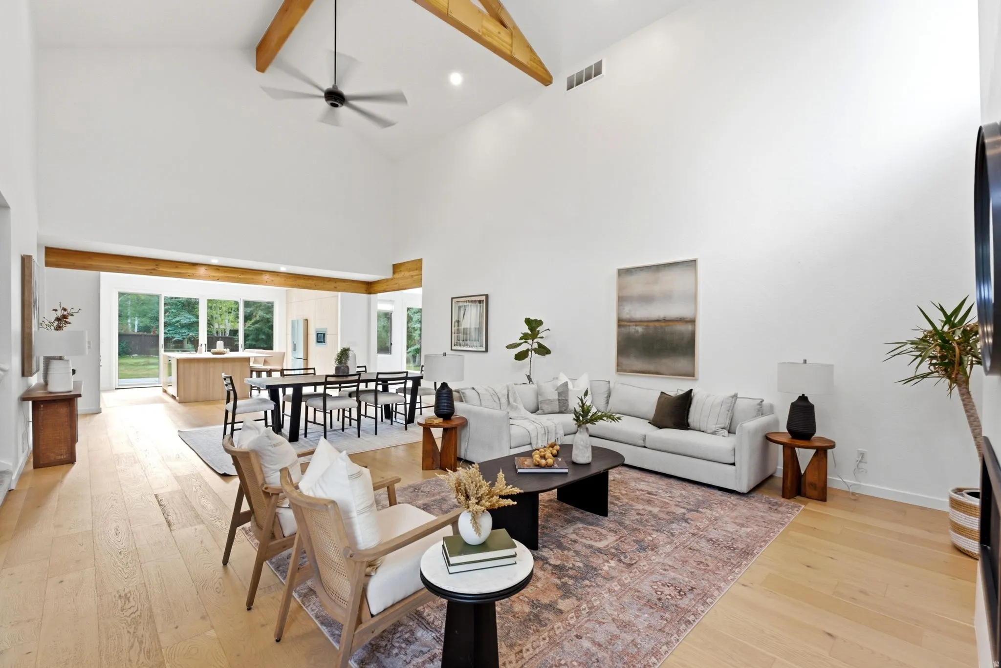 Vaulted ceilings with exposed wood beams, light wood-finish flooring, a contemporary ceiling fan, and sliding glass doors