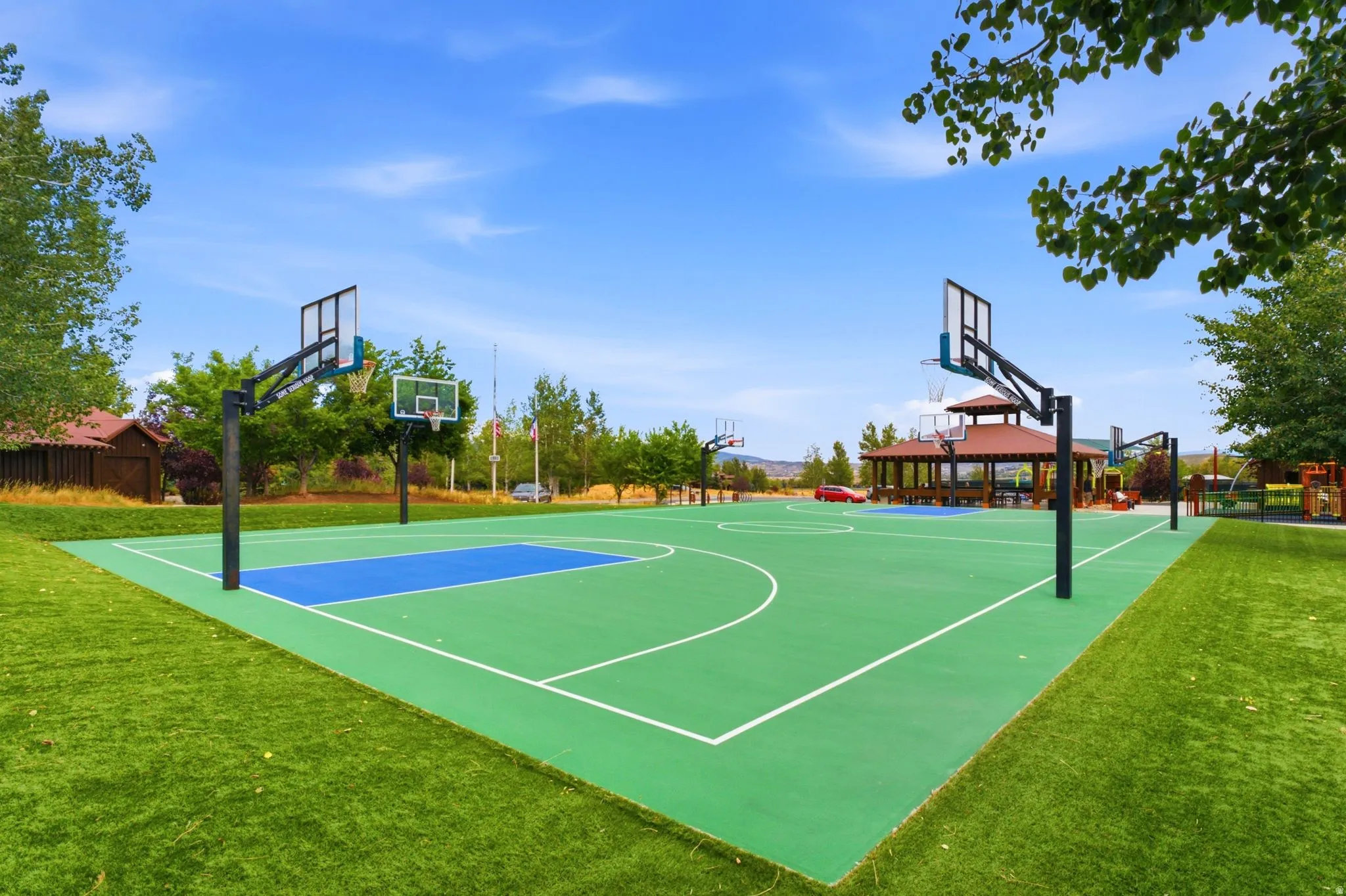 Multi-sport court with vibrant green and blue surfacing, multiple basketball hoops, and surrounding artificial turf