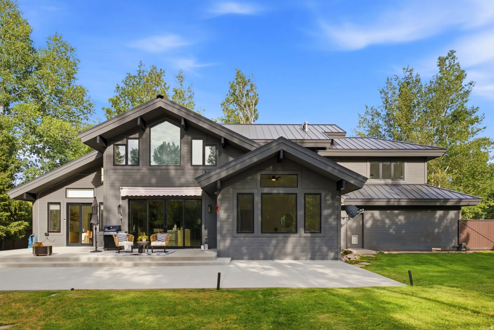 Modern exterior with gray siding, a standing seam metal roof, and an expansive concrete patio