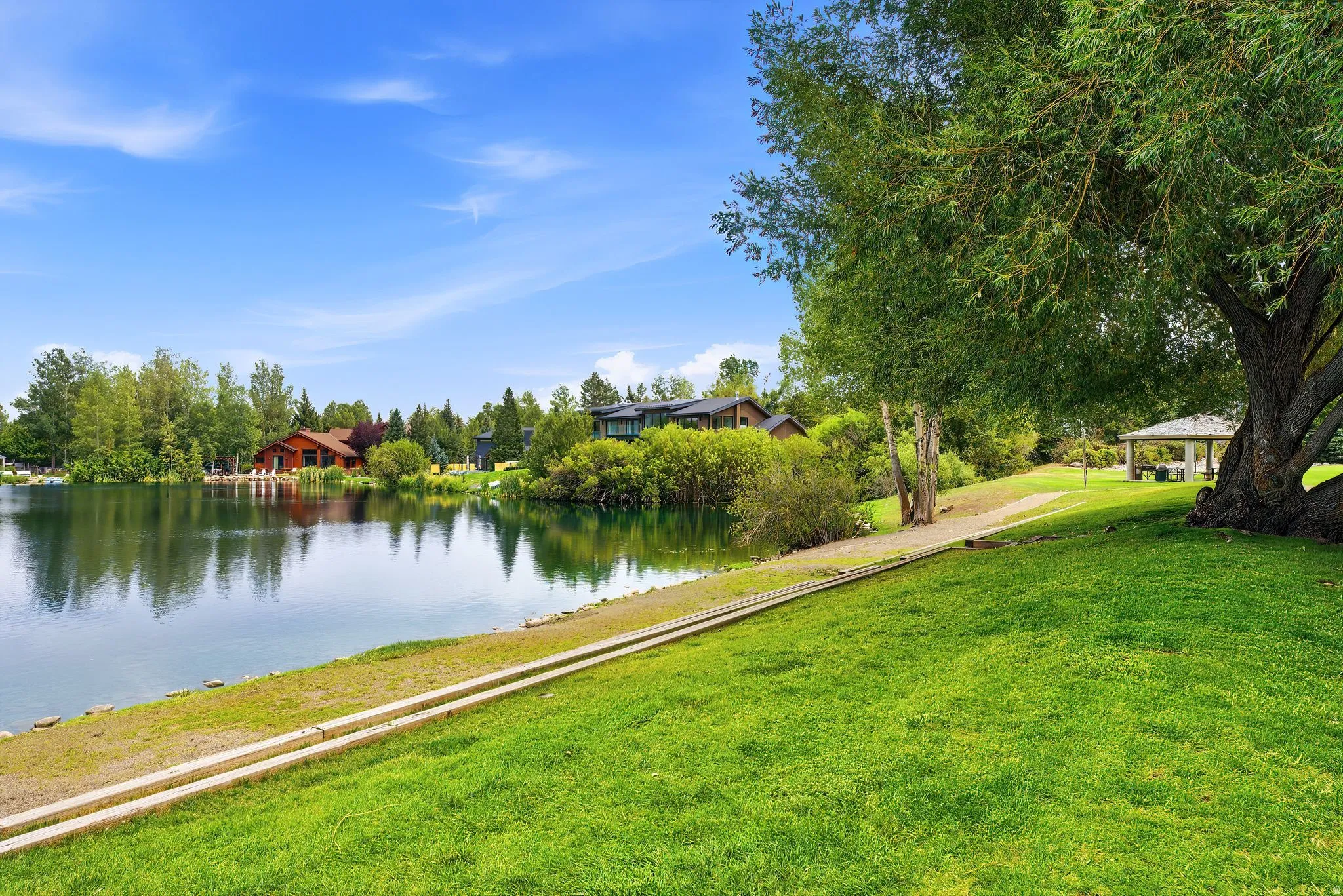 Expansive green lawn sloping to a tranquil body of water, bordered by mature trees and a white gazebo