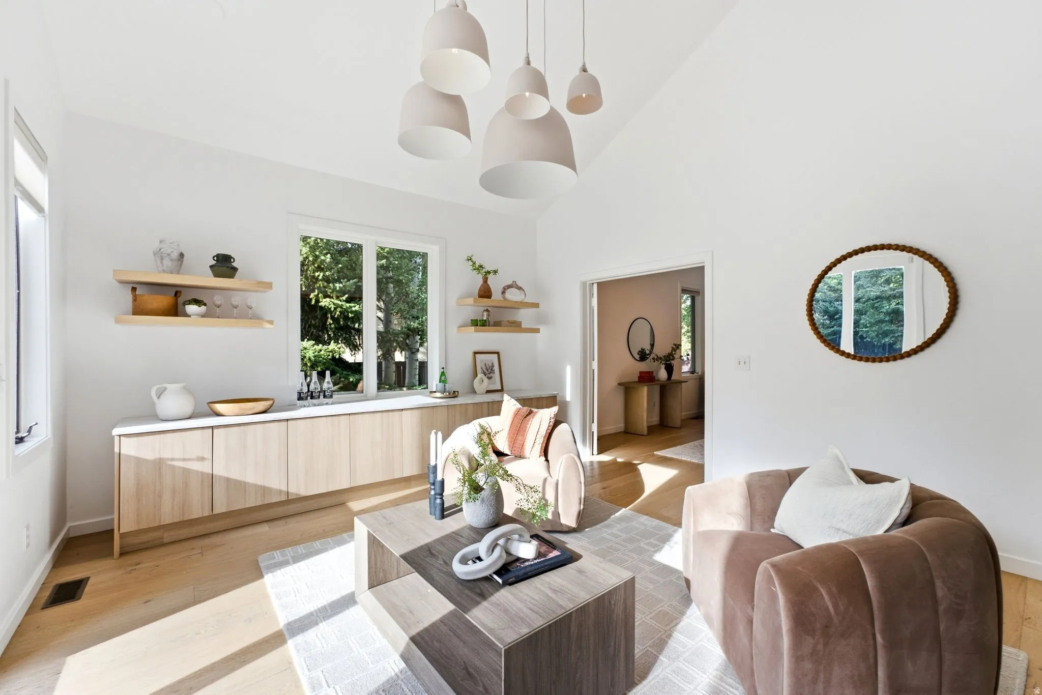 Vaulted ceiling with pendant lighting, light wood-finish flooring, built-in cabinetry with a light-toned countertop, and floating wood shelving
