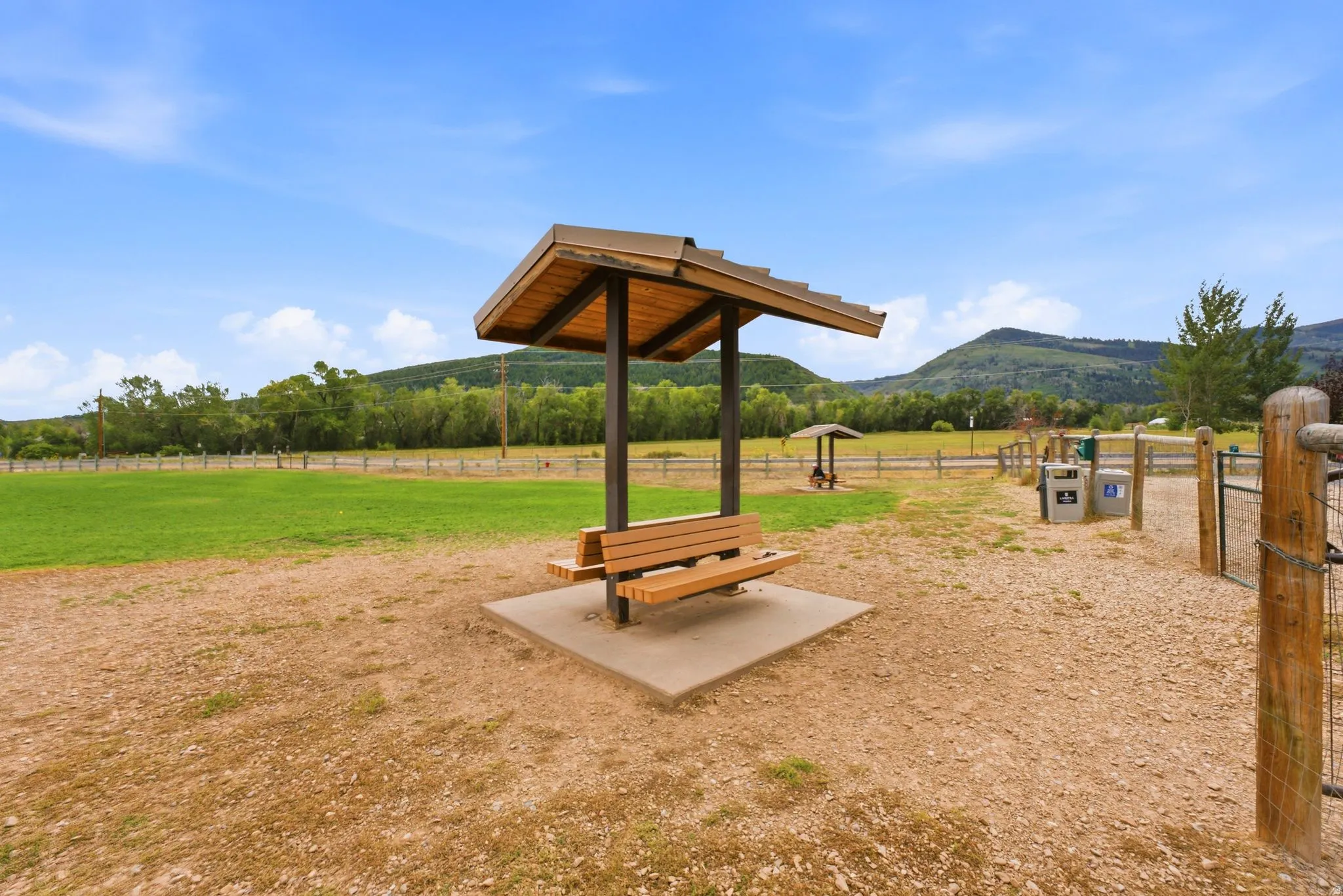 Expansive outdoor space featuring a covered bench, gravel ground cover, and a fenced perimeter