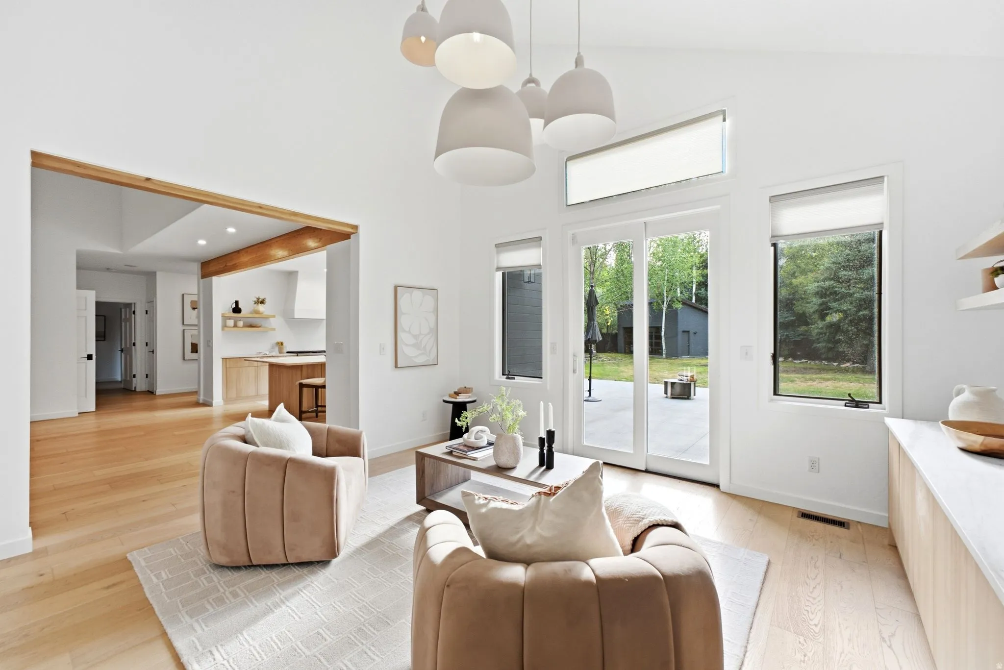 Vaulted ceiling with modern pendant lighting, light wood-finish flooring, sliding glass doors to outdoor patio, and a wood beam architectural feature