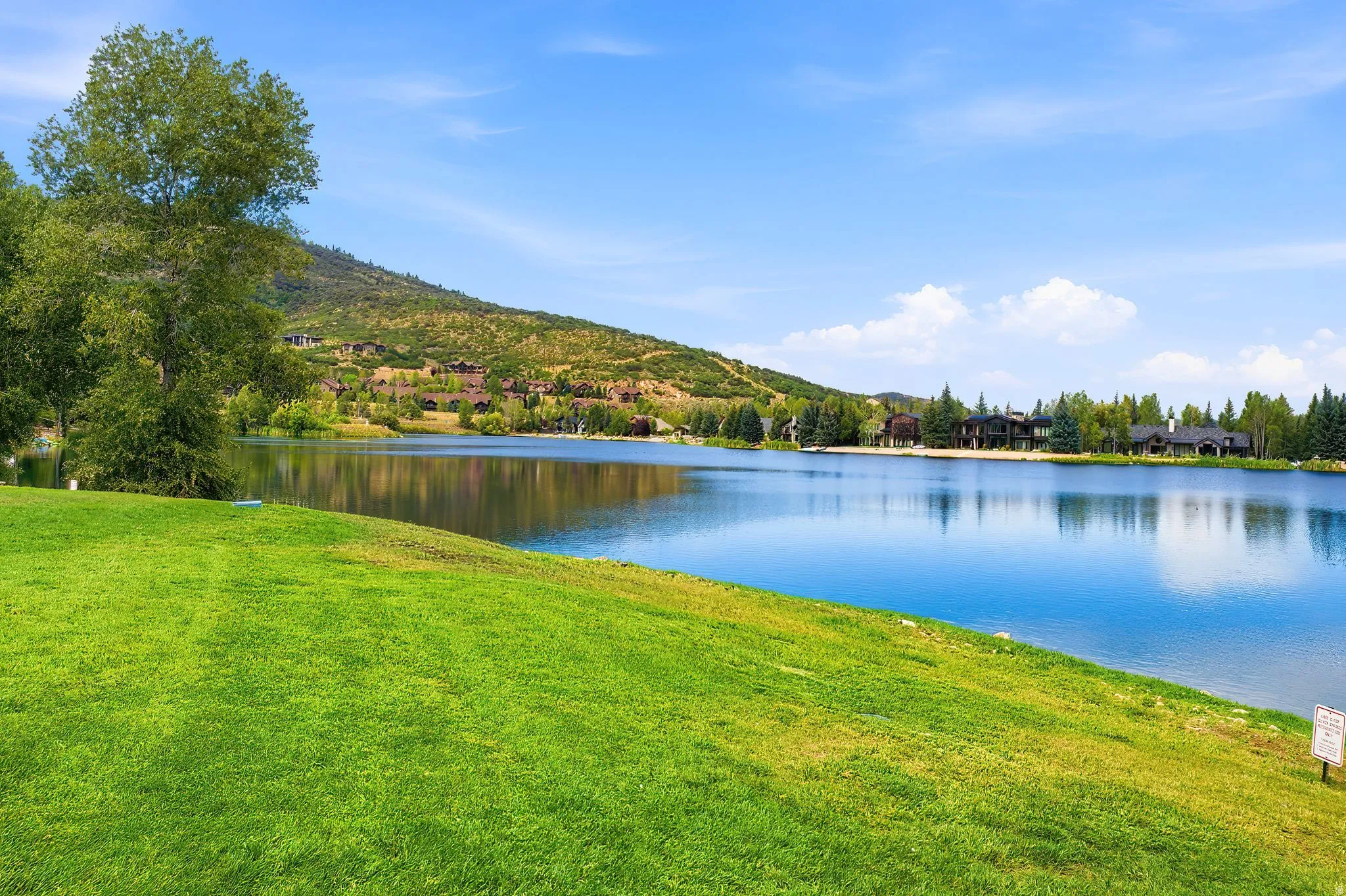 Lush green lawn with mature trees, offering extensive lake frontage with mountain backdrop