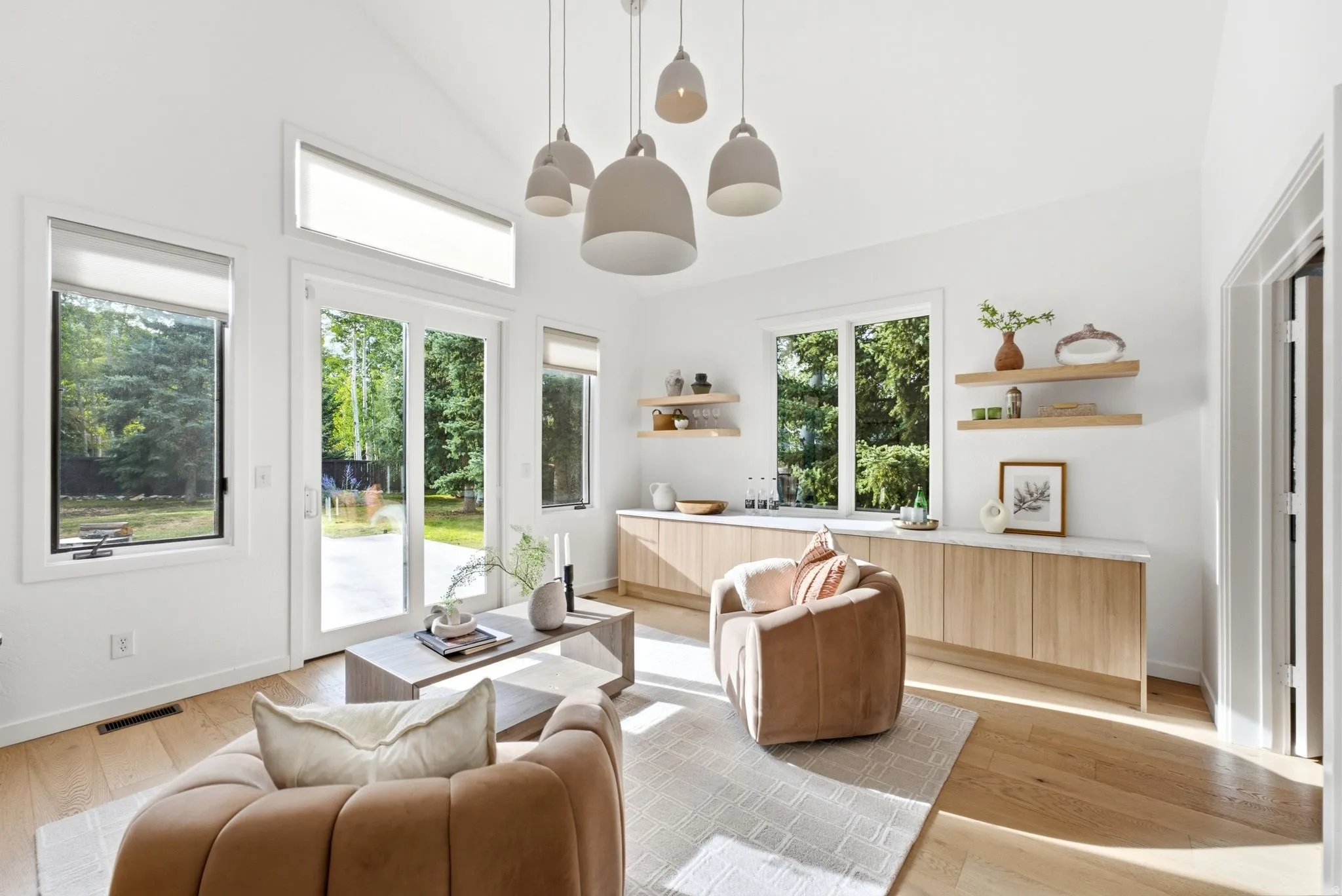 Vaulted ceiling with pendant lighting, light wood-finish flooring, built-in lower cabinetry with a light-toned countertop, and multiple windows with transoms