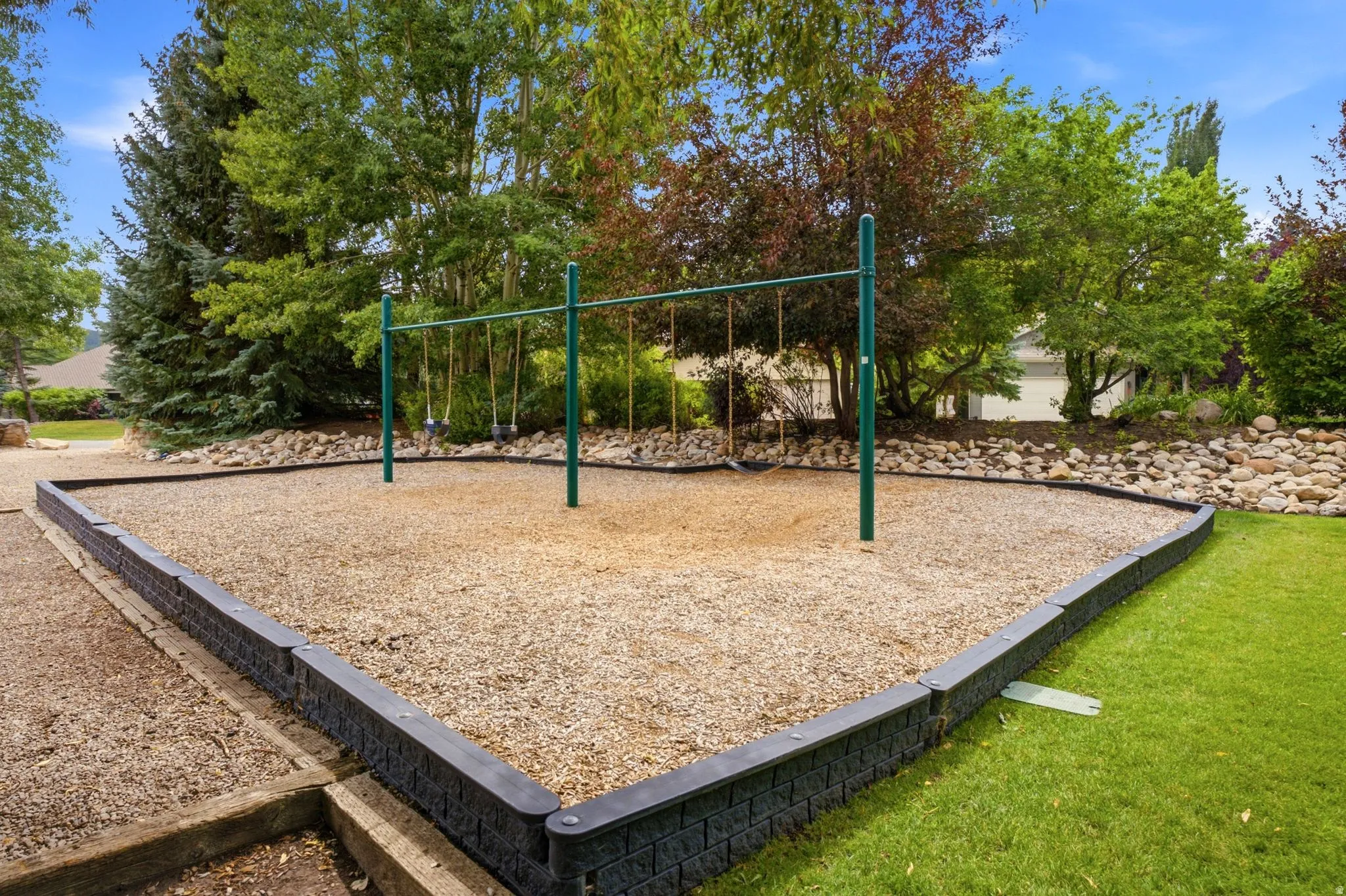Dedicated play area with a swing set, wood chip surfacing, and a stone retaining wall